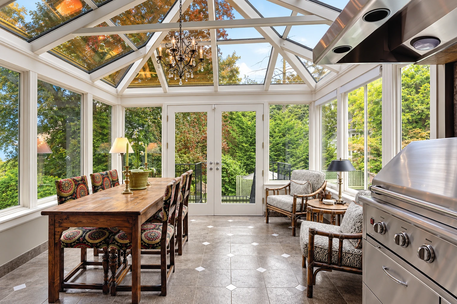 Bright four-season sunroom with a glass roof, dining table, lounge chairs and stainless-steel grill overlooking leafy trees.