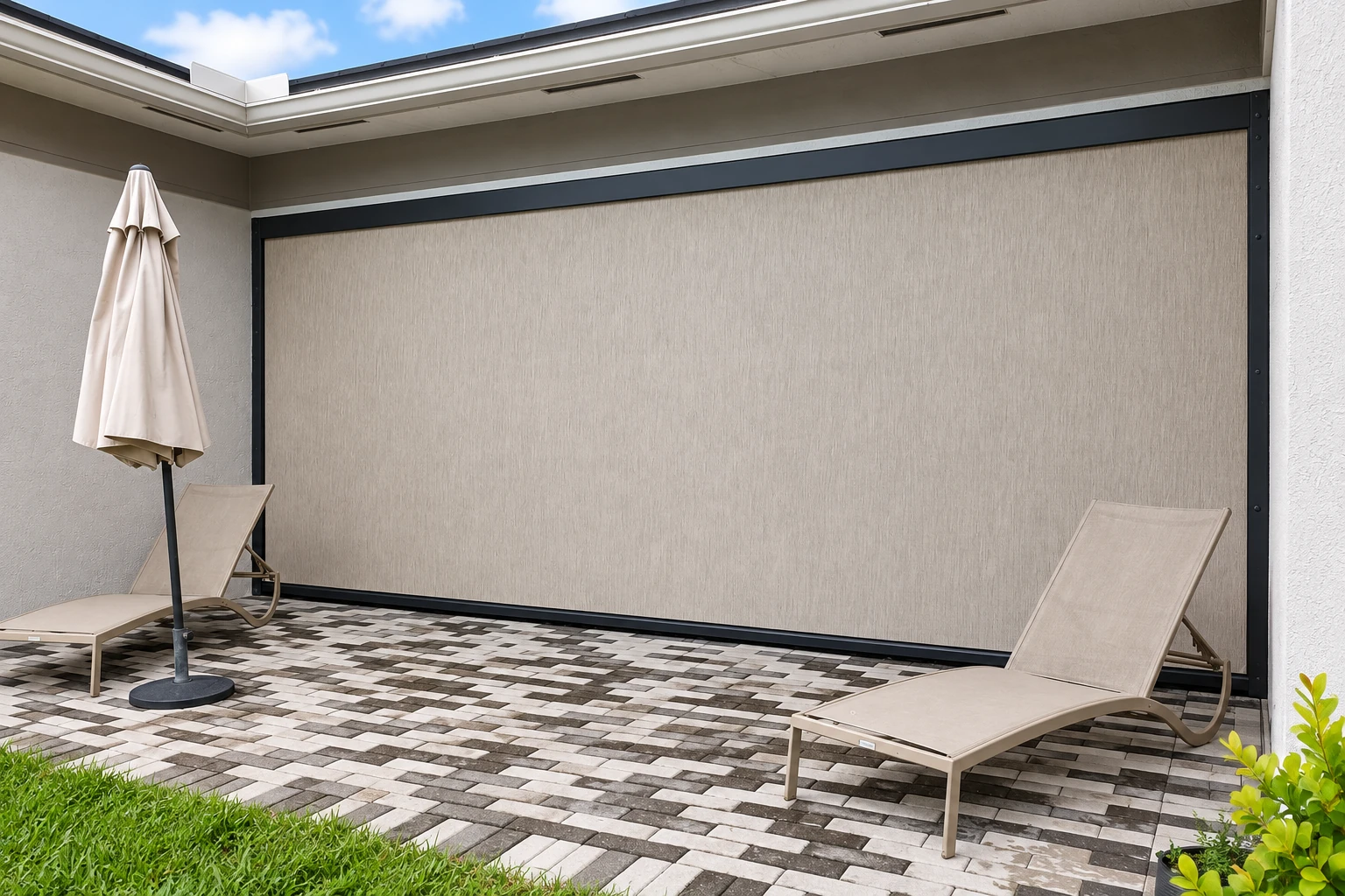 Covered patio with a large retractable shade screen, two lounge chairs, and a paved floor.