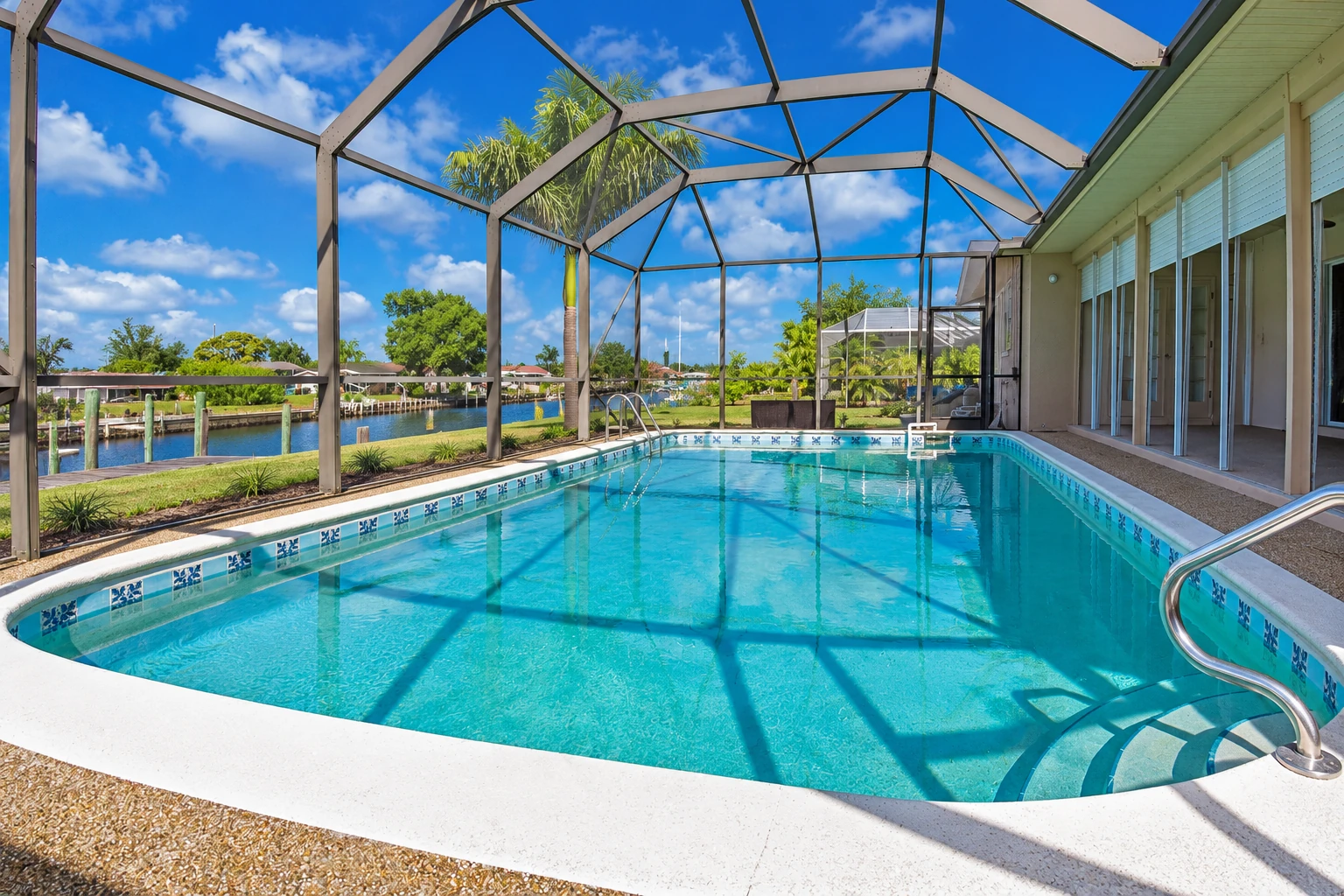Screened-in pool enclosure with a high peaked metal frame, turquoise water and a canal beyond.