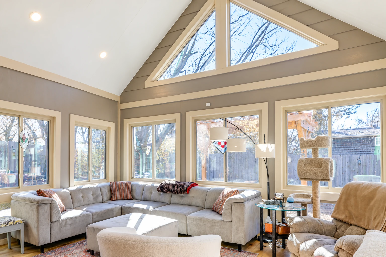 Bright sunroom living area with a high vaulted ceiling, triangular clerestory windows, and a sectional sofa.